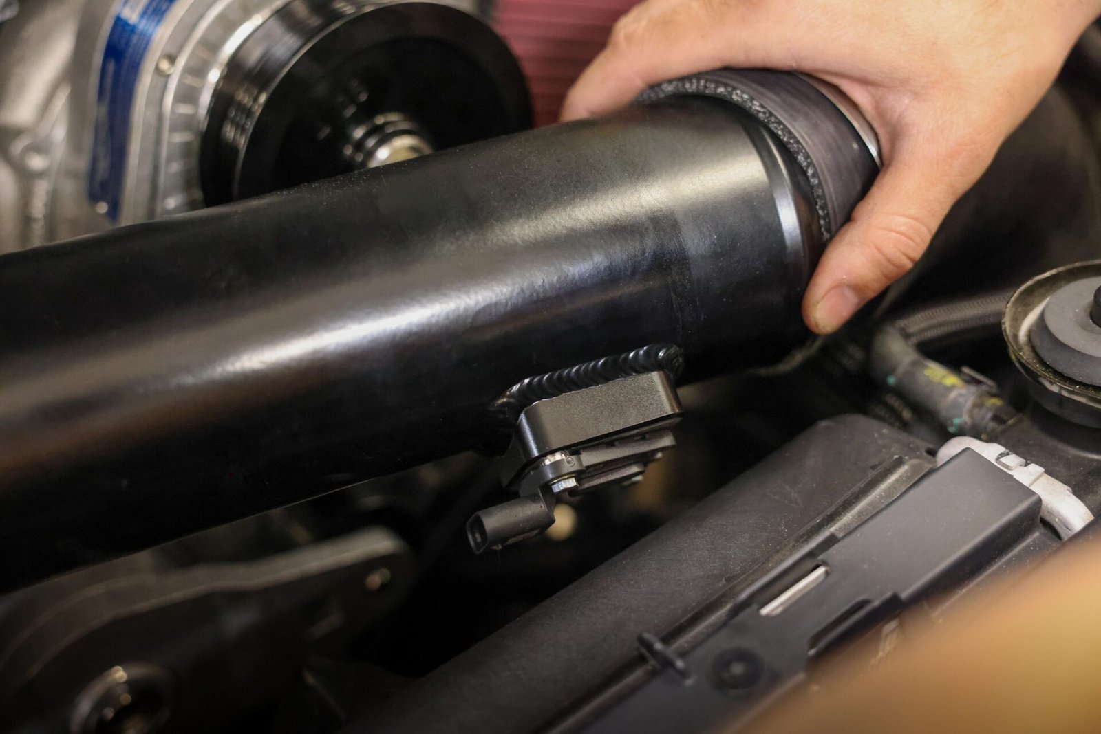 Hand seating the black charge pipe with its blow-through MAF sensor next to the ProCharger supercharger head unit